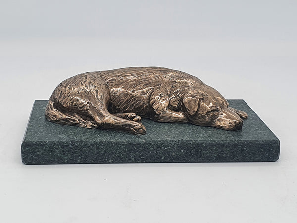 A sculpture in bronze of a Labrador Retriever sleeping, on a Lakeland slate base.