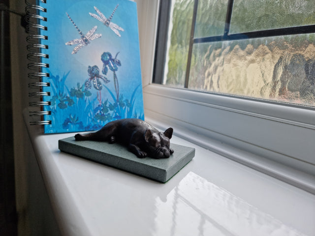 Sculpture of a French Bulldog lying on a window sill.