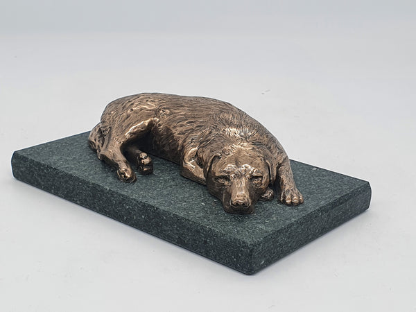 A sculpture in bronze of a Labrador Retriever sleeping, on a Lakeland slate base.