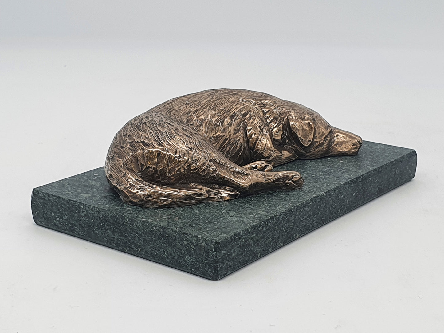 A sculpture in bronze of a Labrador Retriever sleeping, on a Lakeland slate base.