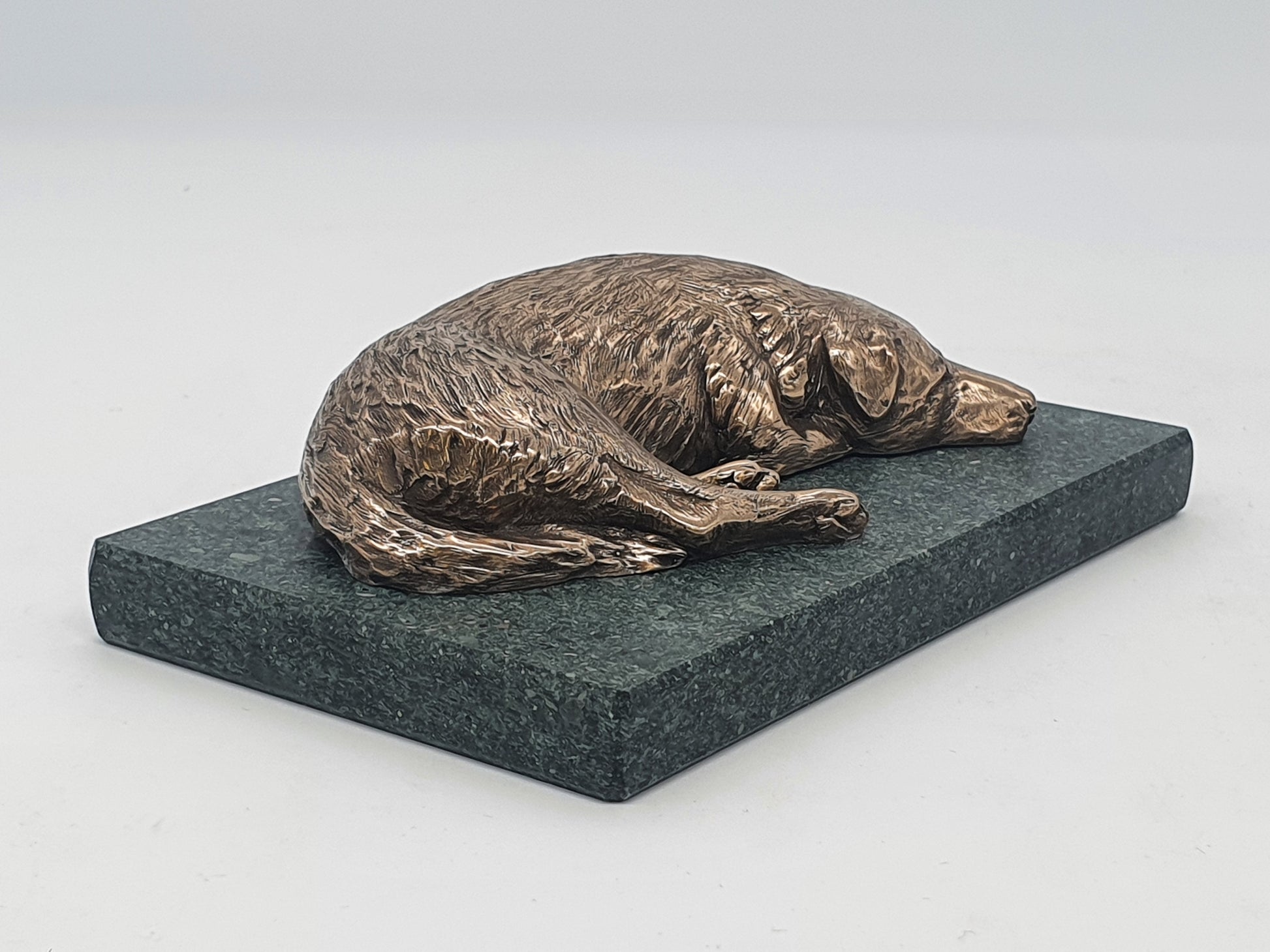 A sculpture in bronze of a Labrador Retriever sleeping, on a Lakeland slate base.
