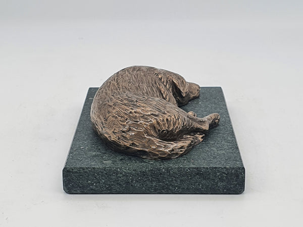 A sculpture in bronze of a Labrador Retriever sleeping, on a Lakeland slate base.