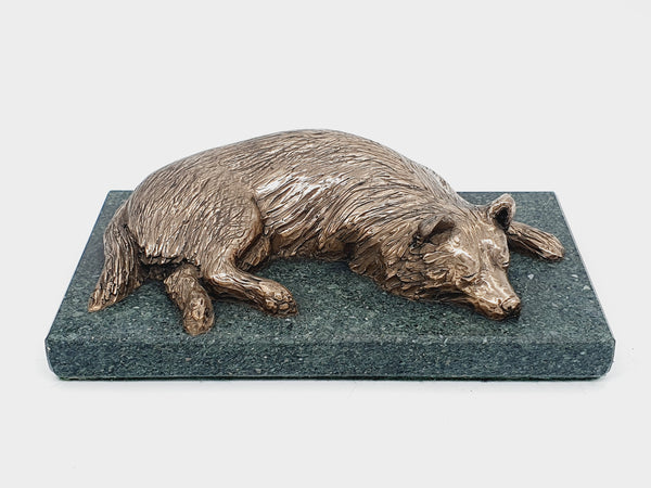 A bronze sculpture of a sleeping Border Collie on a Lakeland slate base