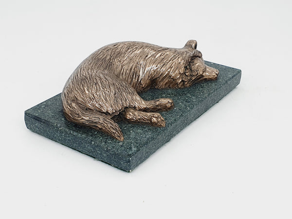 A bronze sculpture of a sleeping Border Collie on a Lakeland slate base