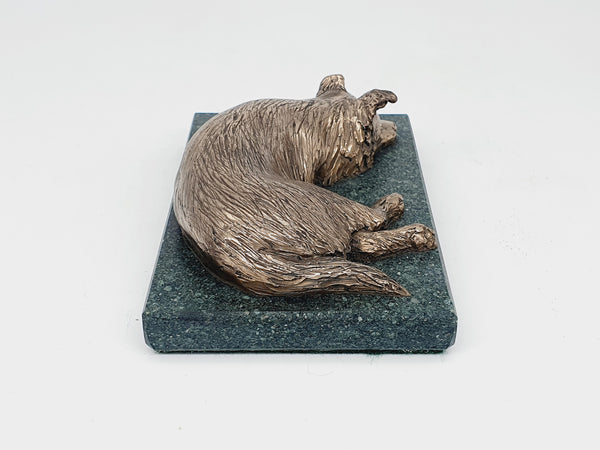 A bronze sculpture of a sleeping Border Collie on a Lakeland slate base