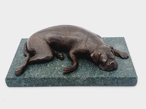 A sculpture of a sleeping Boxer Dog in bronze on a Lakeland slate base