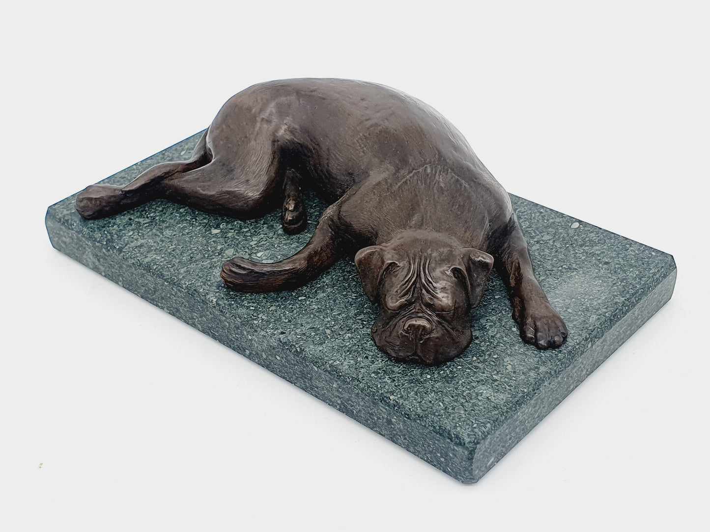 A sculpture of a sleeping Boxer Dog in bronze on a Lakeland slate base