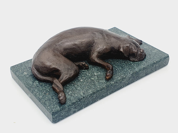 A sculpture of a sleeping Boxer Dog in bronze on a Lakeland slate base