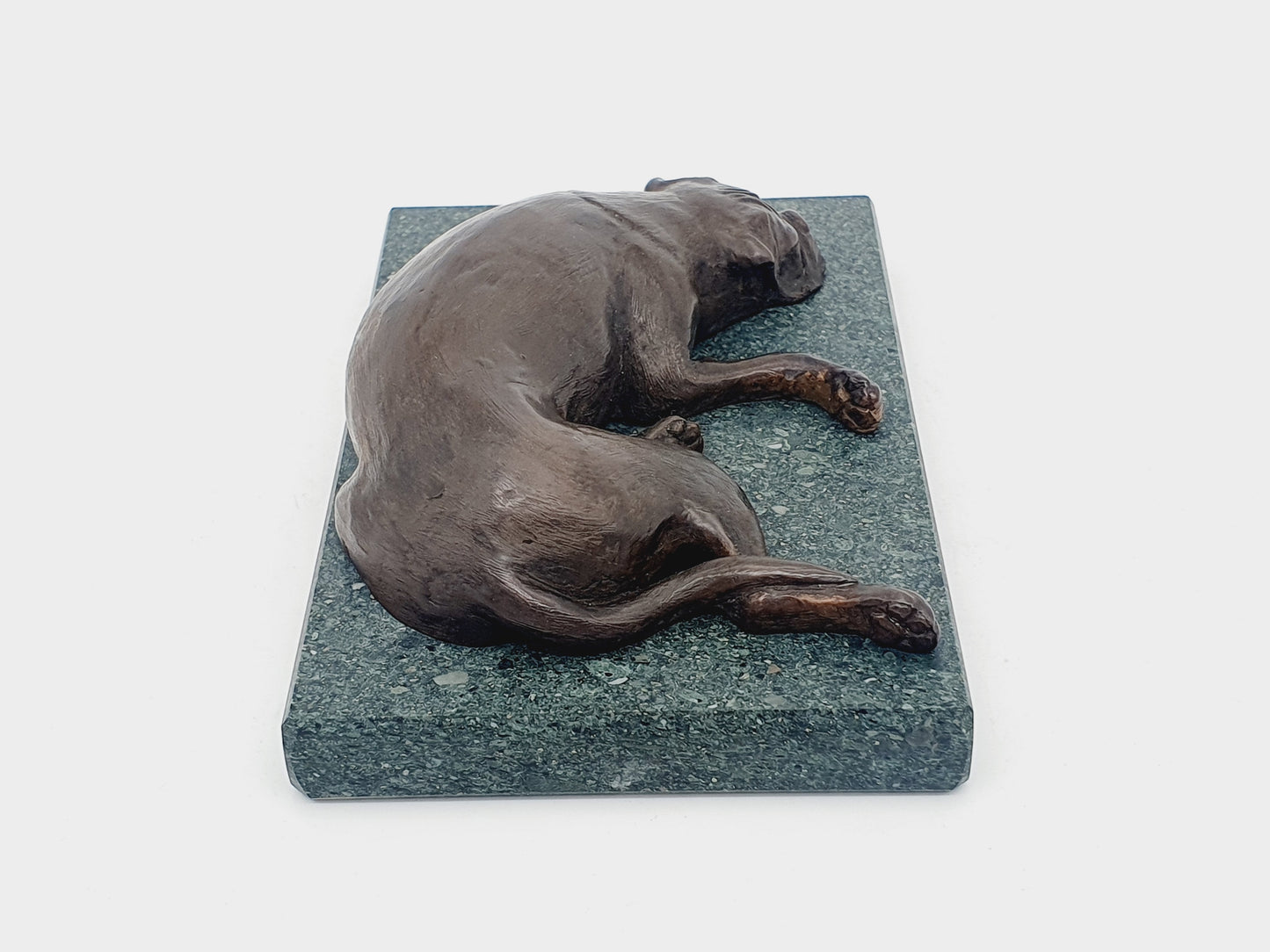 A sculpture of a sleeping Boxer Dog in bronze on a Lakeland slate base