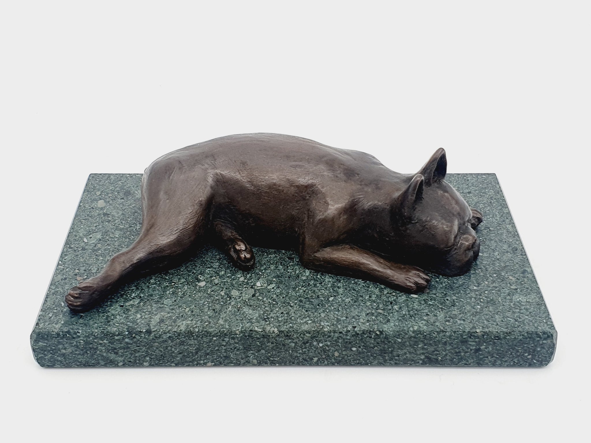 A sculpture of a sleeping Boston Terrier in bronze on a Lakeland slate base