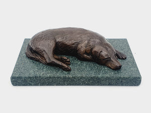 A sculpture in bronze of a Labrador Retriever sleeping, on a Lakeland slate base.