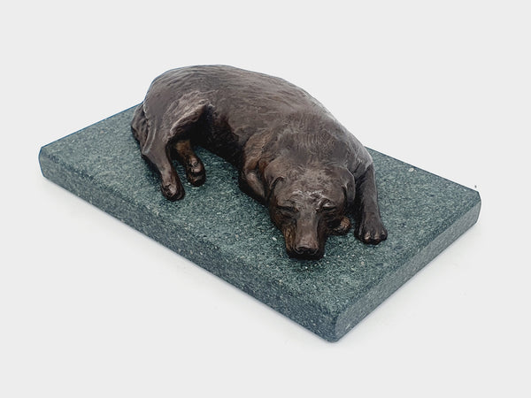 A sculpture in bronze of a Labrador Retriever sleeping, on a Lakeland slate base.