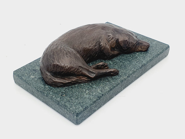 A sculpture in bronze of a Labrador Retriever sleeping, on a Lakeland slate base.