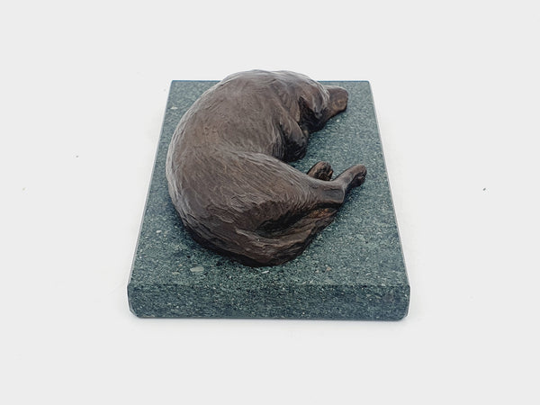 A sculpture in bronze of a Labrador Retriever sleeping, on a Lakeland slate base.